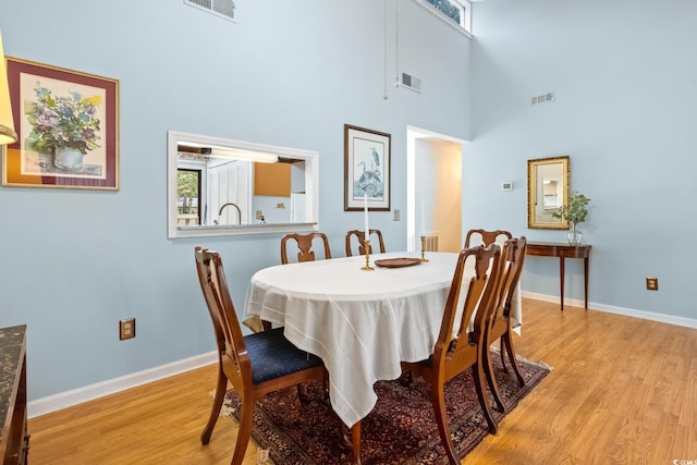 dining space with light hardwood / wood-style flooring and a towering ceiling