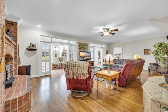 living room with a wood stove, ceiling fan, light hardwood / wood-style flooring, and ornamental molding