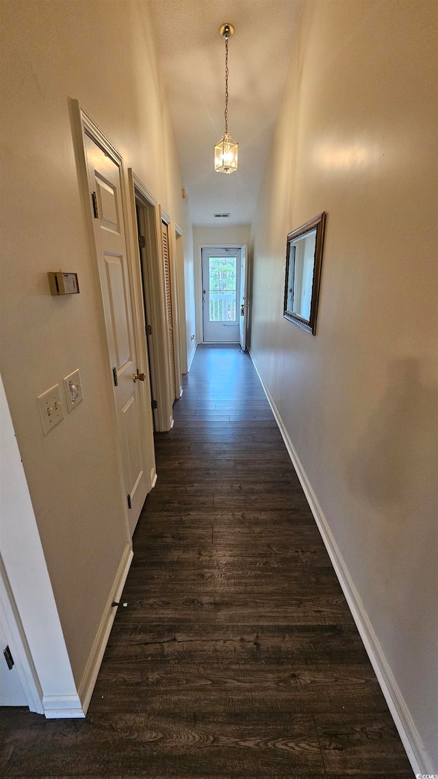 hallway with lofted ceiling, dark wood-type flooring, and a chandelier