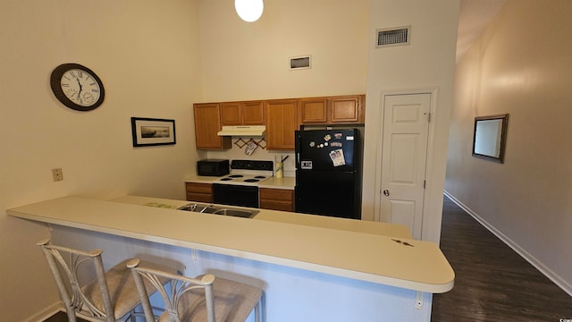 kitchen featuring sink, dark wood-type flooring, kitchen peninsula, a kitchen bar, and black appliances