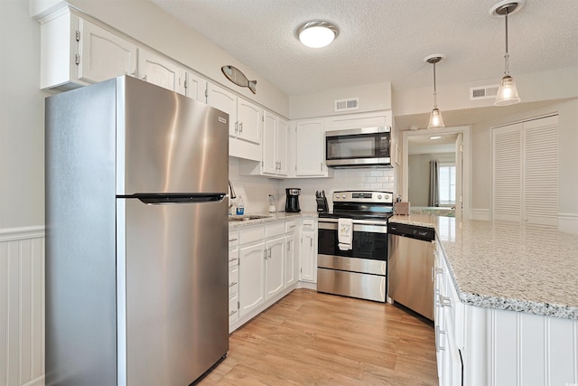 kitchen with light wood-type flooring, a textured ceiling, appliances with stainless steel finishes, decorative light fixtures, and white cabinetry