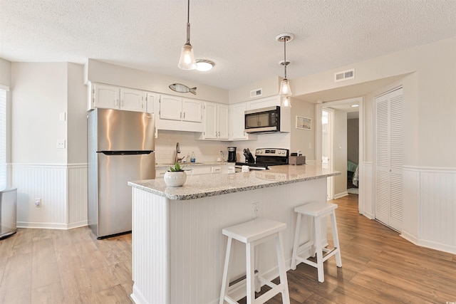 kitchen with light hardwood / wood-style floors, light stone counters, white cabinetry, and stainless steel appliances