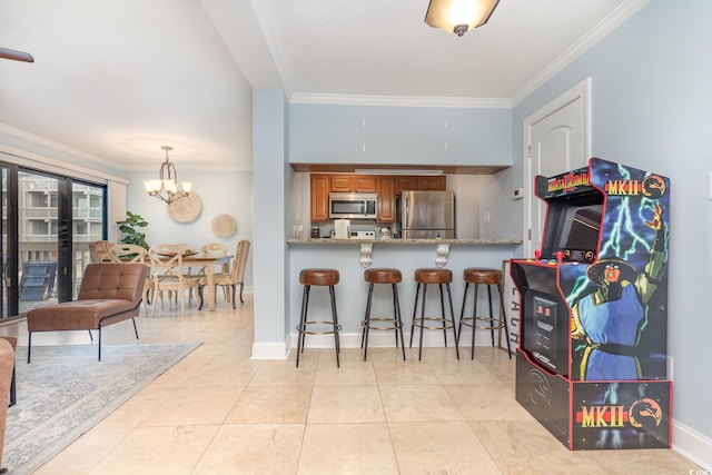 kitchen featuring stainless steel appliances, light stone counters, decorative light fixtures, a kitchen bar, and ornamental molding