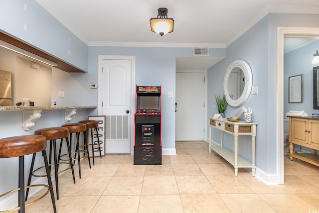 kitchen featuring light tile patterned flooring, stainless steel refrigerator, crown molding, and a breakfast bar area