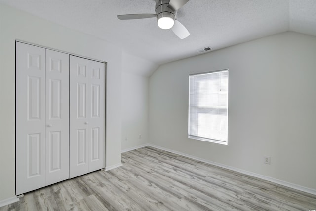 unfurnished bedroom with ceiling fan, a textured ceiling, vaulted ceiling, a closet, and light wood-type flooring