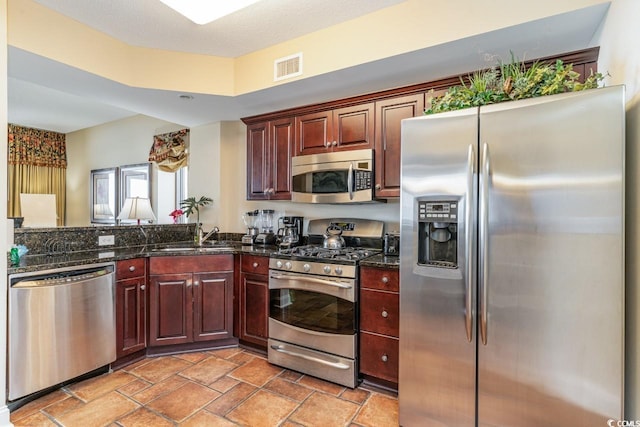 kitchen with a textured ceiling, dark stone countertops, sink, and stainless steel appliances