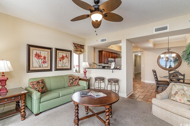 living room featuring carpet flooring, ceiling fan with notable chandelier, crown molding, and a textured ceiling