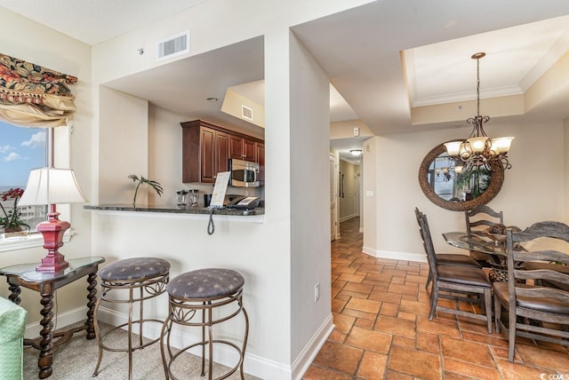 kitchen with kitchen peninsula, a breakfast bar, crown molding, a chandelier, and hanging light fixtures