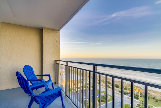 balcony at dusk featuring a water view and a view of the beach