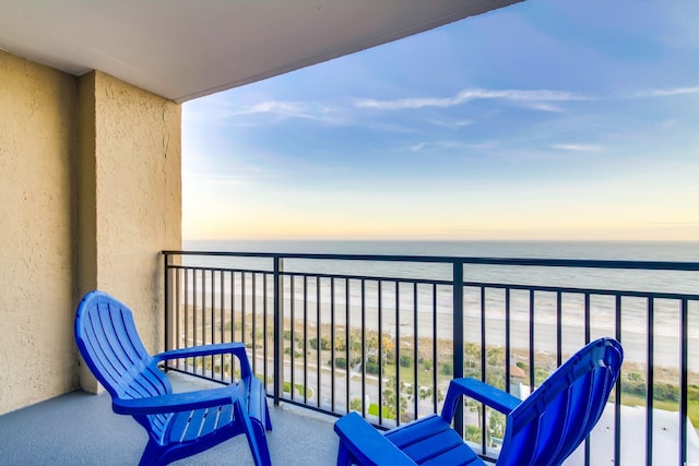 balcony at dusk featuring a view of the beach and a water view