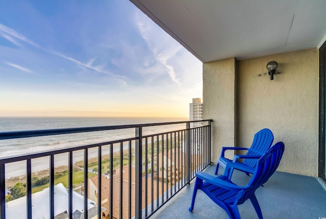 balcony at dusk featuring a beach view and a water view