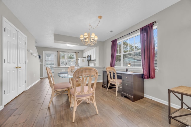 dining area with an inviting chandelier, a healthy amount of sunlight, a textured ceiling, and light wood-type flooring