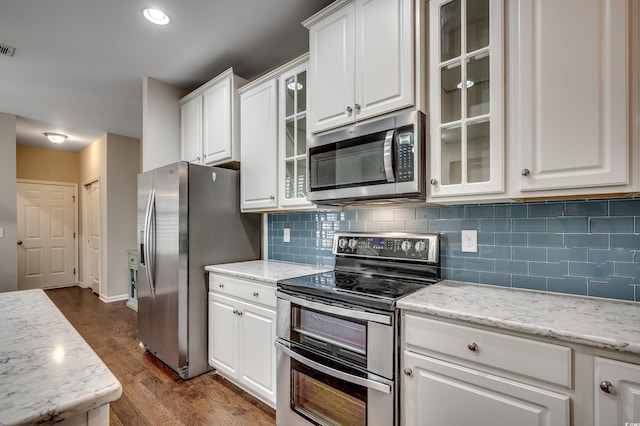 kitchen featuring dark hardwood / wood-style flooring, backsplash, light stone counters, stainless steel appliances, and white cabinetry