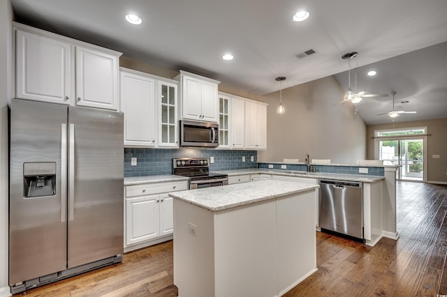 kitchen with appliances with stainless steel finishes, vaulted ceiling, hardwood / wood-style floors, a kitchen island, and hanging light fixtures