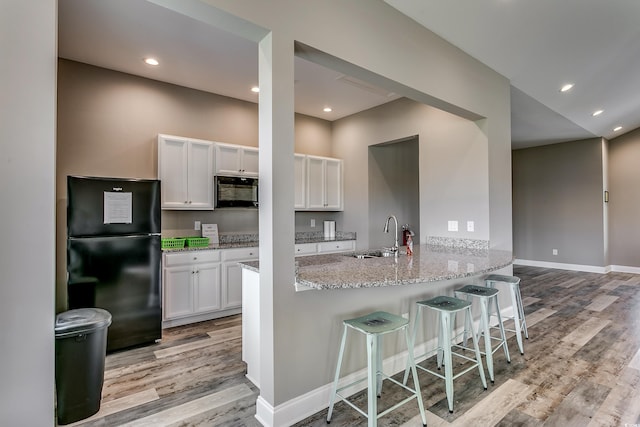 kitchen with kitchen peninsula, light wood-type flooring, sink, black appliances, and white cabinets