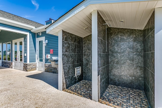 bathroom featuring wood walls, tile walls, tiled shower, and french doors