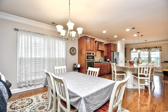 dining space with sink, ornamental molding, dark wood-type flooring, and an inviting chandelier