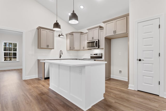 kitchen with hardwood / wood-style flooring, stainless steel appliances, a kitchen island, decorative light fixtures, and vaulted ceiling