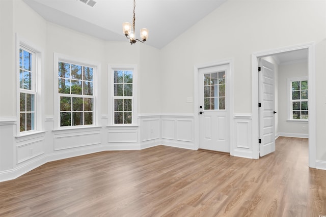 unfurnished dining area featuring vaulted ceiling, plenty of natural light, a notable chandelier, and light hardwood / wood-style floors