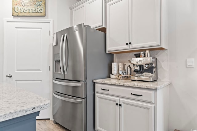 kitchen featuring white cabinetry, light stone countertops, light hardwood / wood-style flooring, stainless steel refrigerator with ice dispenser, and backsplash