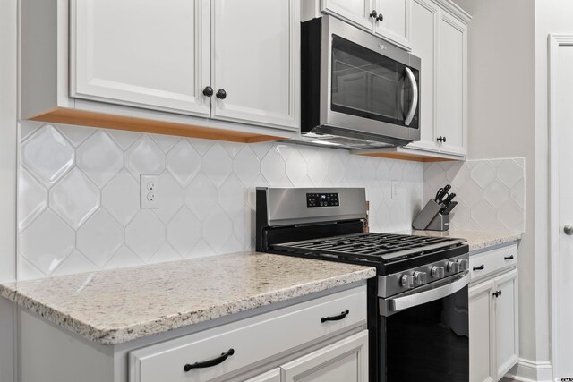 kitchen with stainless steel appliances, light stone countertops, and white cabinets