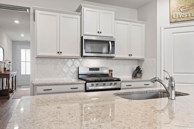 kitchen with hardwood / wood-style floors, white cabinets, sink, light stone countertops, and appliances with stainless steel finishes