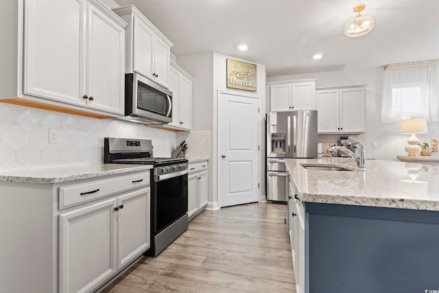 kitchen with white cabinetry, sink, light stone counters, light hardwood / wood-style floors, and appliances with stainless steel finishes