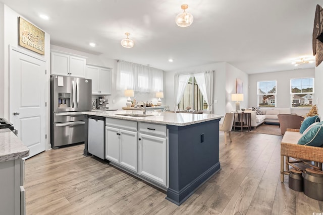 kitchen with light stone countertops, appliances with stainless steel finishes, a center island with sink, white cabinets, and light hardwood / wood-style floors