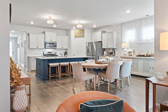 kitchen with white cabinets, a center island with sink, dark wood-type flooring, and appliances with stainless steel finishes