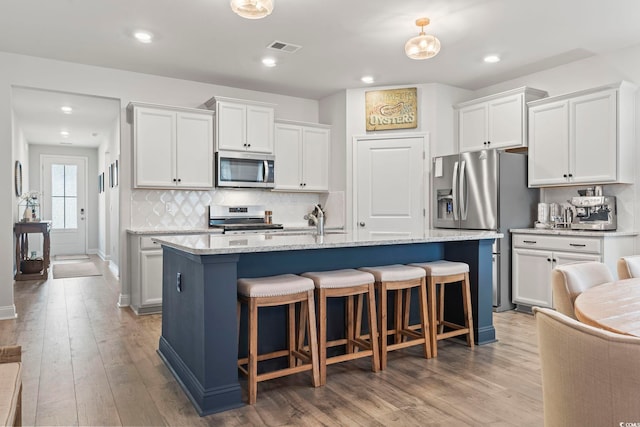 kitchen featuring wood-type flooring, appliances with stainless steel finishes, white cabinetry, and an island with sink