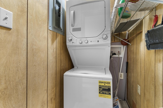 clothes washing area featuring stacked washing maching and dryer and wood walls