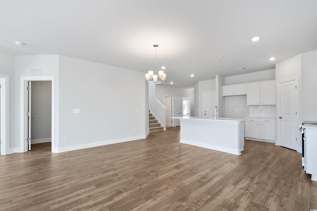 kitchen with open floor plan, a kitchen island with sink, light countertops, white cabinetry, and pendant lighting