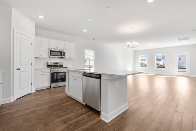 kitchen with light countertops, appliances with stainless steel finishes, a kitchen island with sink, white cabinets, and a sink