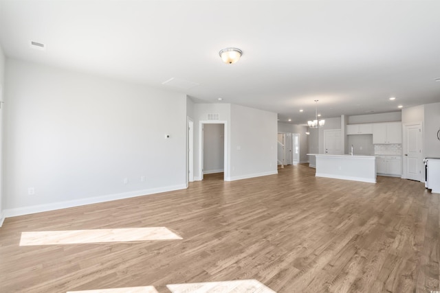 unfurnished living room featuring baseboards, light wood-style flooring, an inviting chandelier, a sink, and recessed lighting