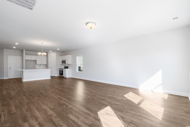 unfurnished living room with a chandelier, dark wood-type flooring, visible vents, and baseboards