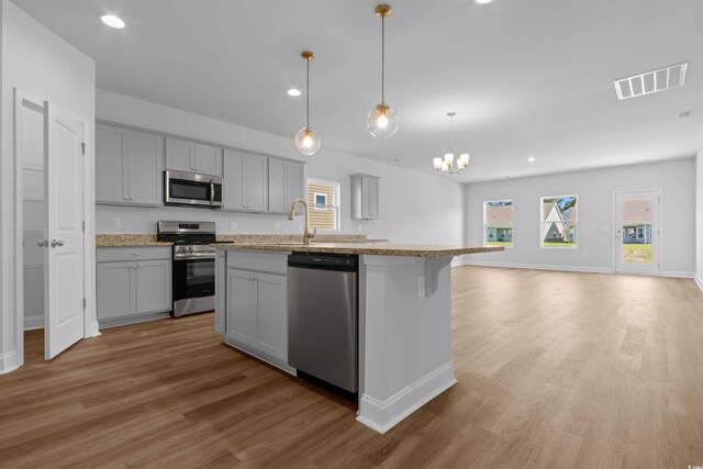 kitchen featuring appliances with stainless steel finishes, a kitchen island with sink, pendant lighting, wood-type flooring, and gray cabinets