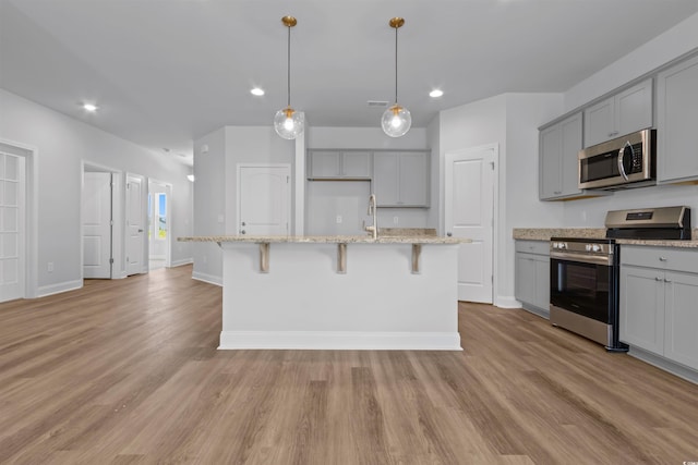 kitchen with gray cabinets, light stone counters, a center island with sink, and stainless steel appliances