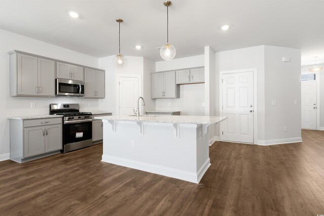 kitchen with hanging light fixtures, a kitchen island with sink, gray cabinetry, and a breakfast bar area