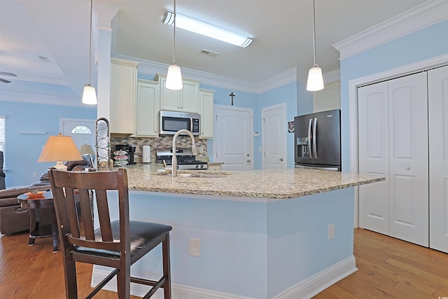 kitchen with crown molding, light wood-type flooring, appliances with stainless steel finishes, decorative light fixtures, and kitchen peninsula