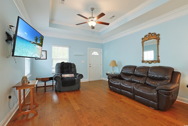 living room featuring hardwood / wood-style floors, ceiling fan, a raised ceiling, and ornamental molding