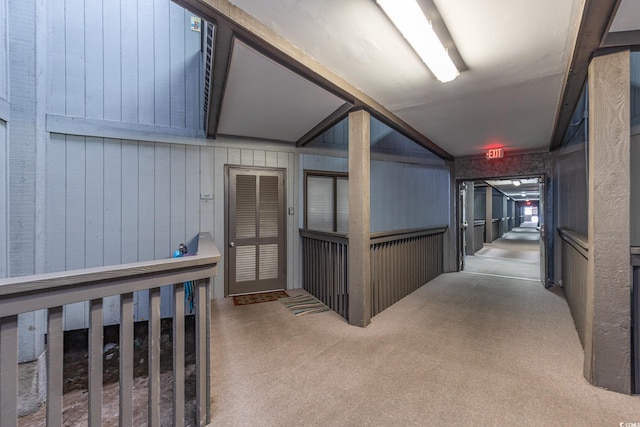 corridor featuring light carpet, lofted ceiling, and wooden walls