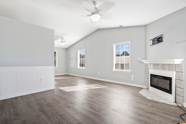 unfurnished living room featuring wood-type flooring, vaulted ceiling, a textured ceiling, a tile fireplace, and ceiling fan