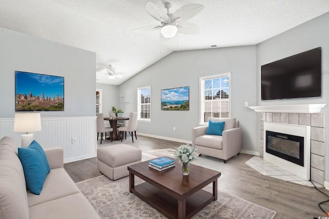 living room featuring light hardwood / wood-style flooring, ceiling fan, a fireplace, a textured ceiling, and vaulted ceiling