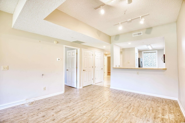 spare room with light hardwood / wood-style floors, a textured ceiling, and track lighting