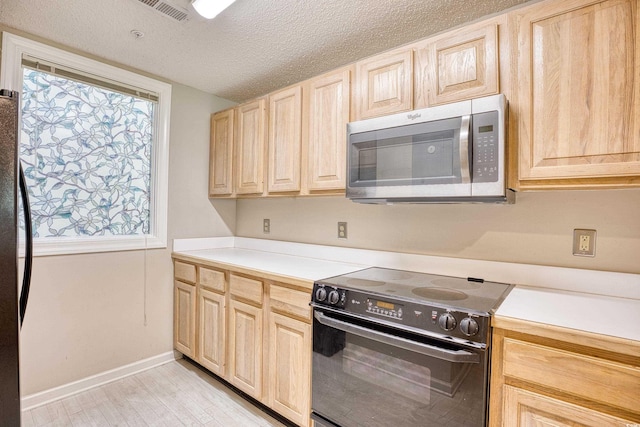 kitchen featuring appliances with stainless steel finishes, a textured ceiling, and light brown cabinetry