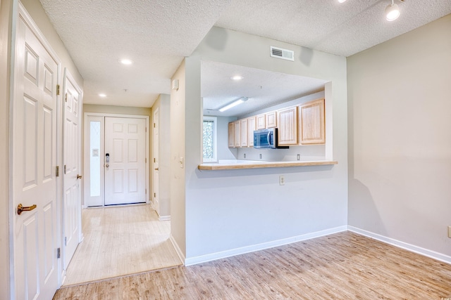 kitchen featuring kitchen peninsula, light brown cabinets, light wood-type flooring, and a textured ceiling