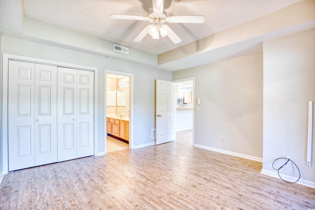 unfurnished bedroom with a raised ceiling, ceiling fan, ensuite bathroom, and a textured ceiling