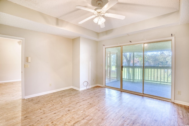 spare room with ceiling fan, light hardwood / wood-style floors, a textured ceiling, and a tray ceiling