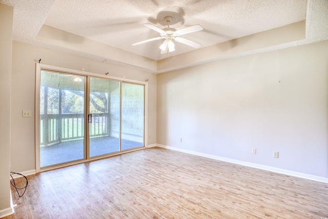 unfurnished room with a raised ceiling, ceiling fan, light hardwood / wood-style floors, and a textured ceiling