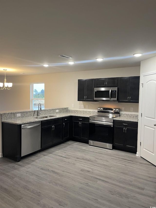 kitchen featuring an inviting chandelier, sink, light hardwood / wood-style flooring, light stone counters, and stainless steel appliances
